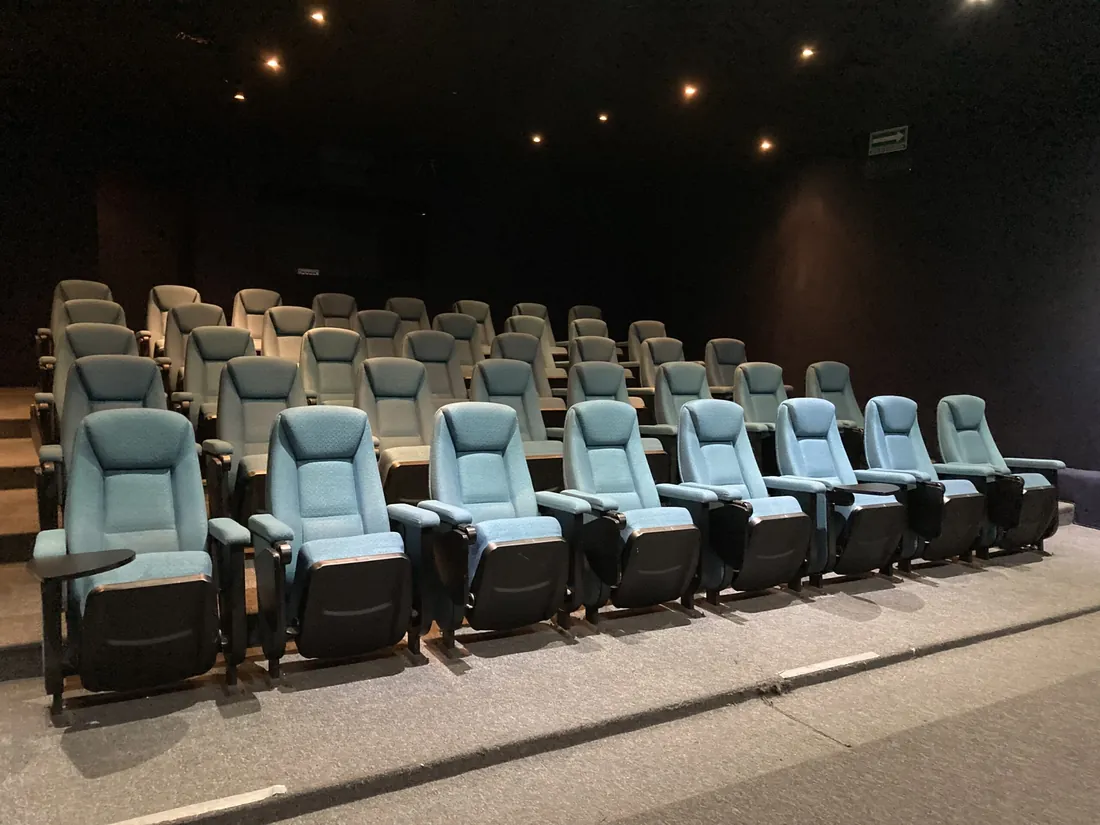 El auditorio del hotel: filas de butacas fijas tapizadas en azul, con mesita de brazo plegable