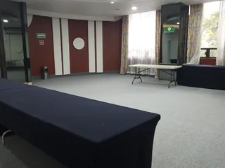 Salón pequeño con una mesa vestida de negro, muro de paneles rojos y un ventanal con cortinas al fondo