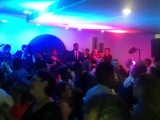 Un evento en marcha: un grupo tocando en la tarima y la pista llena de gente bailando bajo luces de color