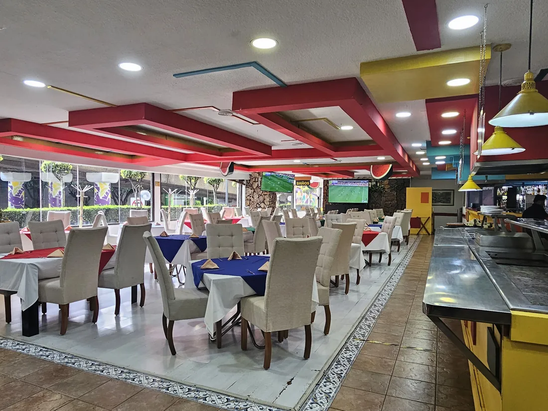 Salón de Real Canto del Agua: vigas rojas en el techo, lámparas amarillas y mesas vestidas frente a los ventanales