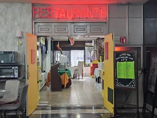 Entrada del restaurante, con el letrero de neón «Restaurante» y el pizarrón del menú del día