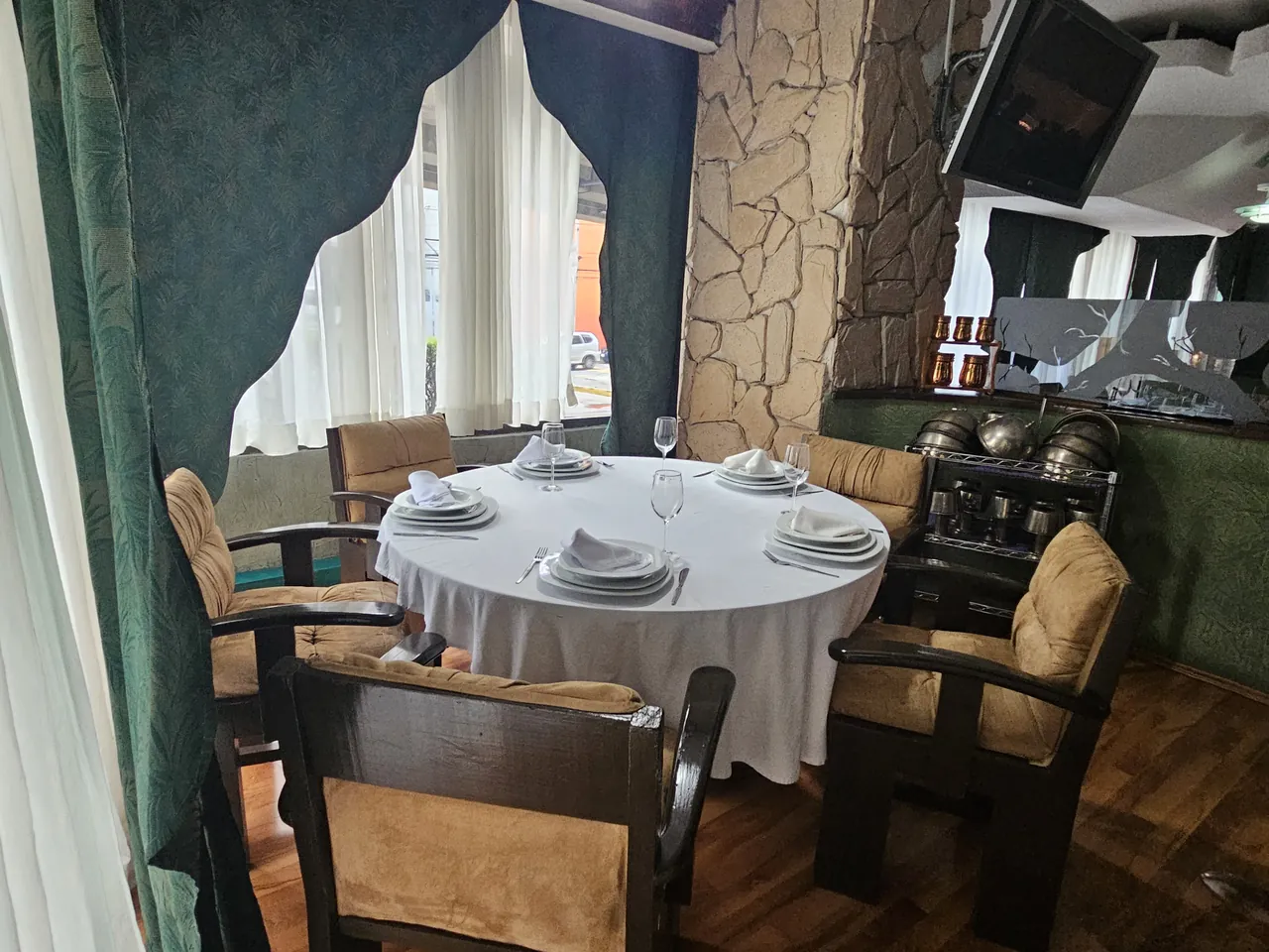 Mesa redonda de La Cava del Duque, vestida con mantel blanco, copas y servilletas dobladas, entre la cortina verde y la columna de piedra